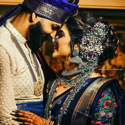 This is our authentic Maharashtrian bridal look. The bride is wearing a traditional silk saree in royal blue with intricate borders, paired with classic silver temple jewelry. The groom complements her in a white kurta and a matching royal blue pagdi.