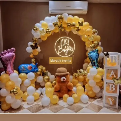 A charming 'Oh Baby' shower decoration with a yellow and white balloon arch, a neon sign, and cute teddy bear and elephant figures. The transparent 'BABY' blocks add a modern touch.