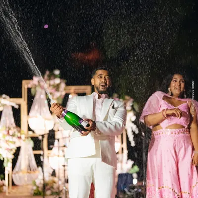 A moment of pure celebration! The groom pops a bottle of champagne at their glamorous outdoor cocktail party.