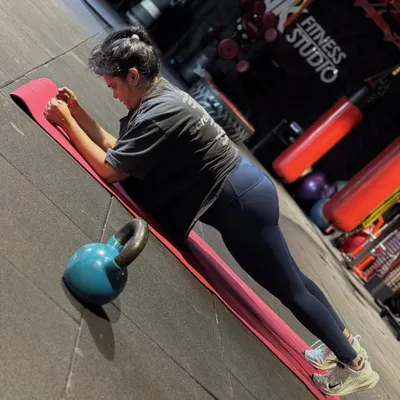 The plank is a fundamental core strengthening exercise. This client is holding a perfect forearm plank, engaging her abs and keeping her body in a straight line from head to heels. A kettlebell is nearby, ready for the next part of her circuit.