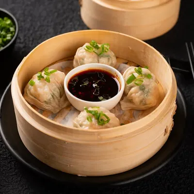 A classic shot of steamed dim sum in a bamboo basket, perfectly styled for an online delivery menu. The image is clean, bright, and clearly shows the customer what they will receive.