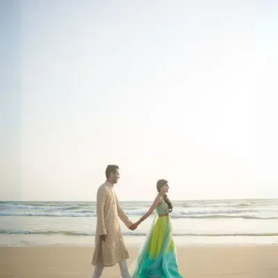 A beautiful, wide-angle shot of a couple walking hand-in-hand on a serene beach, showcasing their connection against the vastness of the ocean.