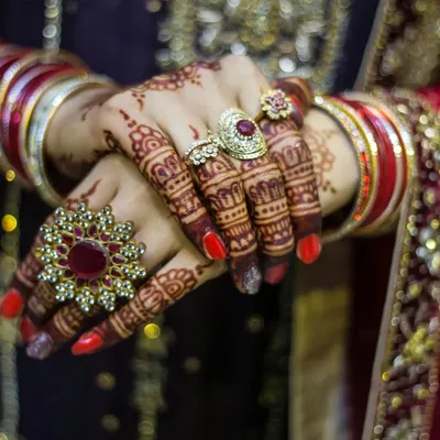 A close-up shot focusing on the bride's hands, showcasing the beautiful bridal rings, bangles, and intricate mehendi design.
