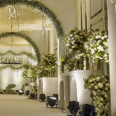 An enchanted forest theme brought to life. This setup features a walkway lined with white structures and massive arrangements of white flowers and greenery, with hanging arches of baby's breath.