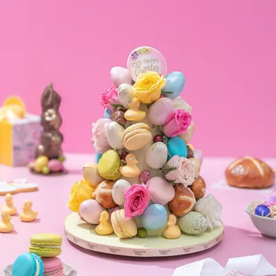 My spectacular Easter Treat Tower, a cone adorned with colorful macarons, mini hot cross buns, fresh roses, and chocolate eggs. It's a stunning centerpiece for any Easter celebration.