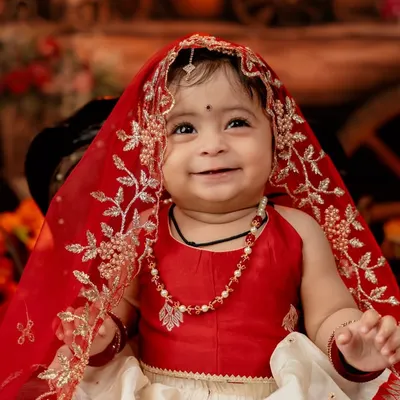 The radiant smile of a little girl dressed in a beautiful red and white traditional outfit. The delicate veil and jewelry complete this stunning portrait.