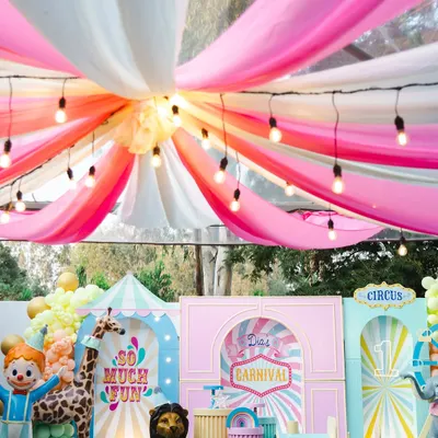 A breathtaking view of Dia's carnival, with colorful draped fabrics and string lights creating a magical big-top tent effect. The backdrop is filled with custom-built circus props and playful characters.
