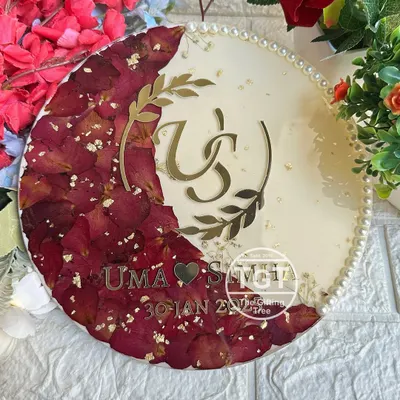 This is a 10-inch round resin frame where I preserved red rose petals from a varmala in a crescent moon shape. A custom couple logo, names, and the wedding date are featured in gold.