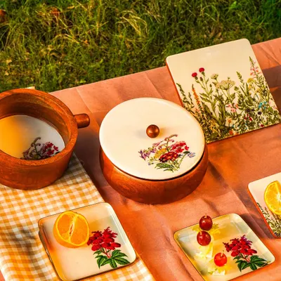 A beautiful outdoor picnic scene featuring hand-painted wooden tableware. The 'golden hour' lighting creates a warm, inviting atmosphere that's perfect for lifestyle brands.