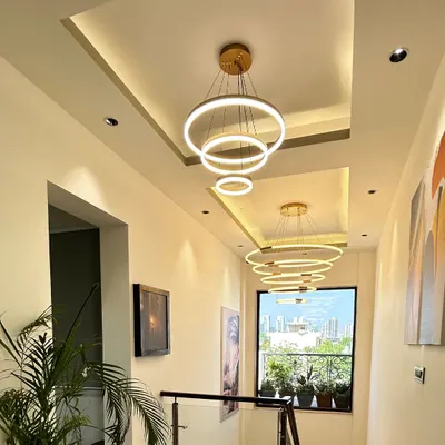 This stunning double-height hallway features a series of modern ring chandeliers and a tray ceiling design, creating a dramatic and luxurious sense of arrival.