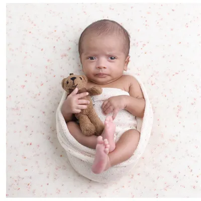 A classic potato sack pose with a twist. This awake and expressive newborn holds a tiny teddy bear, making for an incredibly endearing and memorable portrait.