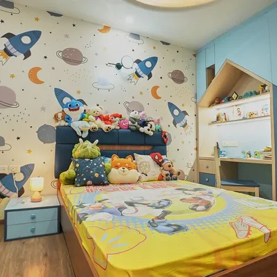 This space-themed bedroom is ready for adventure. The wallpaper is filled with rockets and planets, and the bed is piled high with cuddly friends. The house-shaped study nook is a cozy spot for reading and drawing.