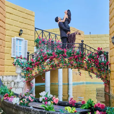 A romantic lift on a flower-adorned bridge over our Venetian canal set. This dynamic shot captures a moment of pure joy and cinematic romance.