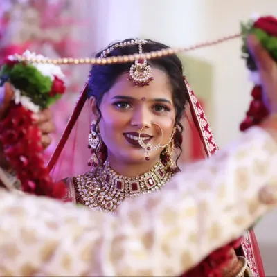 A beautiful moment between the bride and groom during the varmala ceremony. Her makeup is radiant, with a focus on a classic red lip and defined eyes.