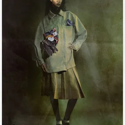 A full-length portrait of the model in an earth-toned outfit, with a collage of magazine clippings attached to her jacket. The painterly, textured background adds a timeless, artistic quality to the modern concept.