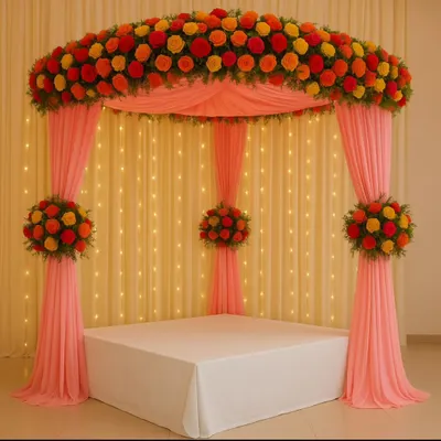 A classic mandap for Navratri or a wedding ceremony. This setup features a canopy of pink drapes topped with a vibrant arch of red, orange, and yellow marigolds, all illuminated by a backdrop of warm fairy lights.