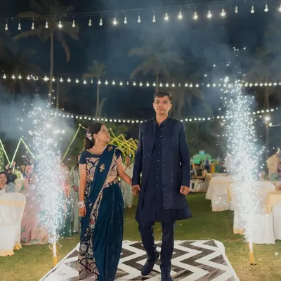 A picture-perfect Sangeet entrance. The couple makes their way down a stylish black-and-white chevron-patterned aisle, flanked by celebratory cold pyro sparklers and set under a canopy of warm string lights.