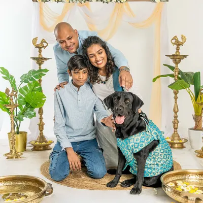 A beautiful family portrait from a Diwali mini-session. The family, dressed in festive attire, gathers around their black Labrador for a perfect holiday photo.