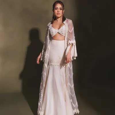 Pearls and tassels make this white indo-western outfit on Nushrratt Bharuccha a true statement piece. The flared pants and detailed cape are perfect for a modern, festive look.