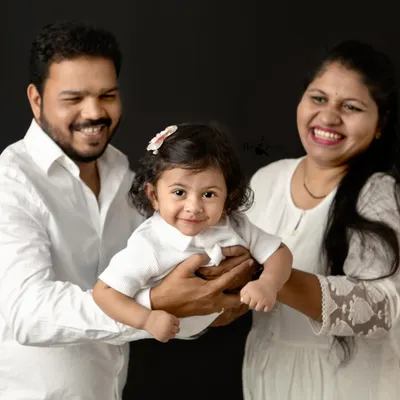 A perfect family portrait, full of laughter and joy. Holding their little one together, this family's happiness is radiant against the classic black studio background.
