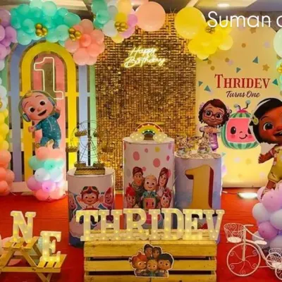 A full Cocomelon themed birthday party setup. This includes a large backdrop with characters, themed plinths for the cake, a gold shimmer wall, and colorful balloon columns.