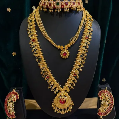 This is a classic temple jewellery set for rent, featuring a choker, a long necklace (haram), and matching jhumka earrings with red and green stones.