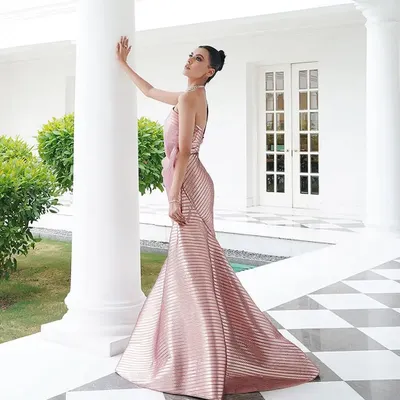 A full-length shot of a stunning metallic pink gown by Amit Aggarwal. The structured, pleated fabric creates a futuristic mermaid silhouette, styled to look statuesque and elegant against the classic architecture.