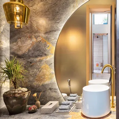 This chic, lounge-like powder room in the Punjabi Bagh residence is clad in exotic stone. A large, off-center backlit mirror and a brass pendant light add a touch of glamour and drama to the space.