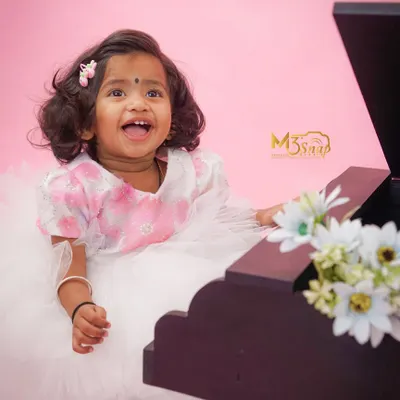 What a happy smile. This little girl is having a great time at her milestone session, playing with a miniature piano against a lovely pink backdrop.