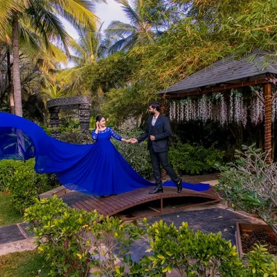 A couple on a wooden bridge surrounded by lush greenery, with the flowing blue dress adding a dramatic splash of color to the natural scene.