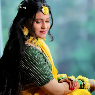 A classic Haldi look. The bride is glowing, with minimal makeup that enhances her natural beauty, perfectly matching her yellow saree and floral jewelry.