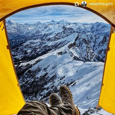 The ultimate room with a view. This is the perspective from inside a tent pitched high in the Himalayas, offering an unparalleled, panoramic vista of a vast, snow-covered mountain range.