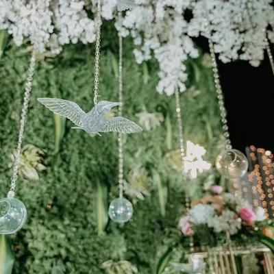 A close-up of a lush green foliage wall with a neon 'Better Together' sign and delicate hanging crystal birds. It's these small, thoughtful details that create a magical atmosphere.