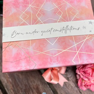 The story often begins with the box itself. This celestial-themed gift box was designed for a baby girl, with a custom sleeve that reads "Born under quiet constellations," setting a magical and personal tone before it's even opened.