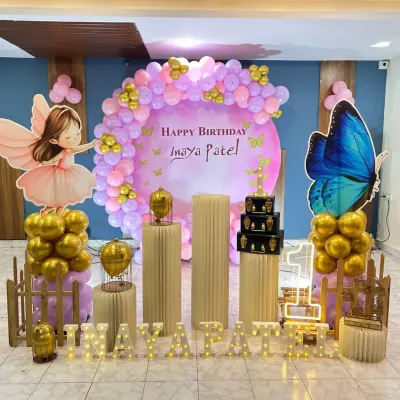A magical fairy and butterfly theme for a first birthday. This setup uses pastel purple and pink balloons, golden chrome accents, life-sized fairy cutouts, and illuminated marquee letters to create an enchanting garden scene.
