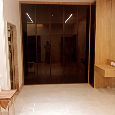 A glimpse into a spacious walk-in wardrobe featuring floor-to-ceiling doors made of dark, reflective glass. This design creates a sense of depth and luxury, with integrated lighting that adds a dramatic effect to the bedroom.