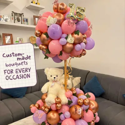 I create custom-made bouquets for every occasion. This one features a sweet teddy bear nestled in a two-tiered arrangement of pink, purple, and rose gold balloons, perfect for a 15th birthday.