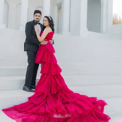 A cinematic portrait of an expecting couple on grand, white steps. The vibrant red of her tiered gown contrasts beautifully with the classic black tuxedo he wears, creating a powerful and romantic image that celebrates their journey to parenthood.