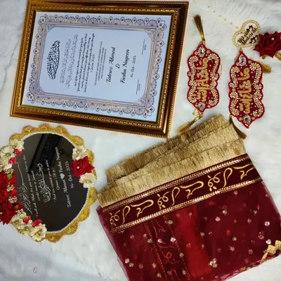 A classic red and gold Nikah set, laid out to show all the matching pieces. This includes a framed certificate, a personalized mirror, a 'Qubool Hai' dupatta, and decorative Iman Zamin bands.
