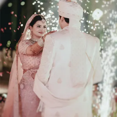 The Varmala ceremony, captured from behind the groom, focusing on the bride's expression as she places the garland. The sparklers add a touch of magic to this pivotal moment.