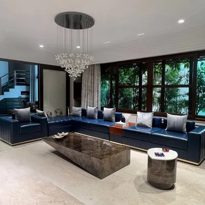 A luxurious living room featuring our bespoke deep blue leather sectional sofa. This piece, with its clean lines and metal base, was crafted to anchor this expansive, light-filled space, as featured in Elle Decor.
