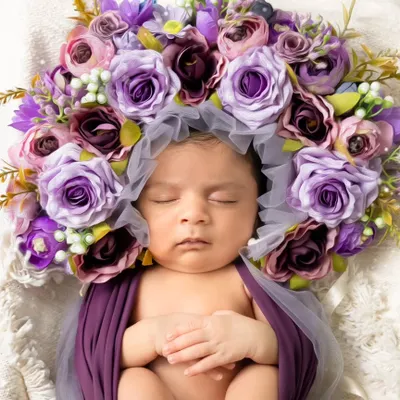 A peaceful newborn rests, swaddled in purple and crowned with a halo of flowers. This is the essence of our newborn artistry sessions.