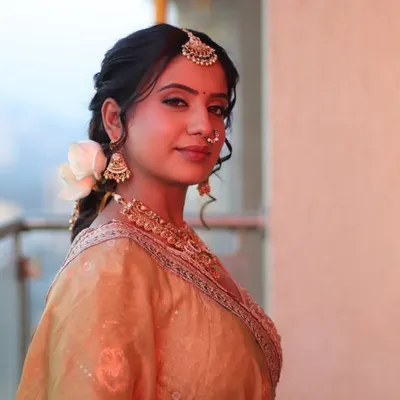 A beautiful portrait of a bride in a golden lehenga. Her hair is styled in a soft, romantic braid with a fresh white rose, perfect for a daytime wedding.