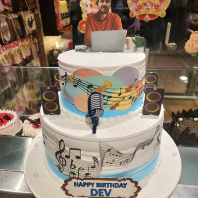 A personalized two-tier cake for a music lover. This design features edible music notes, a microphone, and a custom photo topper of the birthday person.