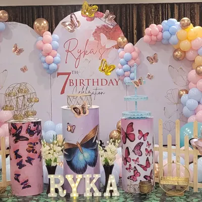 The main stage for a 7th birthday with a butterfly theme. This setup uses pastel pink and blue balloons, butterfly-printed pedestals, and light-up letters for the birthday girl's name.