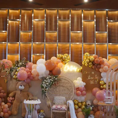 A full view of a 'We Can Bearly Wait' baby shower. The setup features a wicker peacock chair for the mom-to-be, surrounded by a cascade of balloons in earthy tones and a friendly teddy bear.