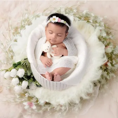 Pure innocence. A newborn baby girl, sleeping peacefully in a white basket, surrounded by soft fabrics and flowers. This is a classic and timeless newborn portrait.