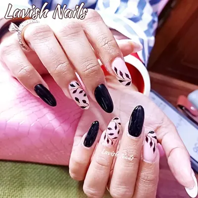 A chic and sophisticated design on almond-shaped nails, featuring a mix of solid black and accent nails with hand-painted black leaves on a sheer pink base.