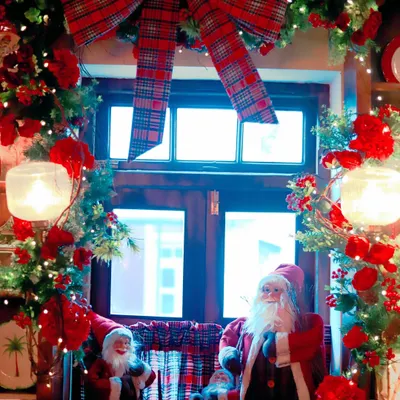 A classic Christmas window display for Scarlett House, featuring Santa figures, a large plaid bow, and a lush garland adorned with red flowers and fairy lights.