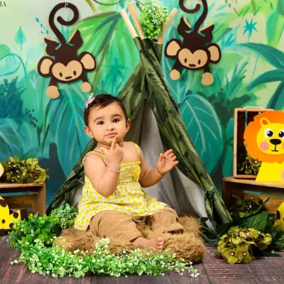 A baby girl sits in a jungle-themed setup, looking curious and sweet among her animal friends.